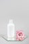 White cosmetic blank bottle and pink flower on mirror, gray background. Natural Organic Spa Cosmetic Beauty Concept Mockup, Front