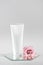 White cosmetic blank tube and pink flower on mirror, gray background. Natural Organic Spa Cosmetic Beauty Concept Mockup, Front