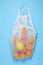 A white cotton string bag with tangerines and lemon lies on a blue background