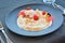 White cream desert with raspberries on black plate in restaurant.
