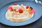 White cream desert with raspberries on black plate in restaurant.