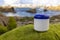 A white cream jar with a blue lid stands on smooth green grass. .