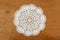 White crochet circle-shaped tablecloth over a wooden background
