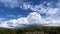 White cumulus clouds in the blue sky over green mountains. Panorama
