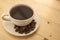 White cup with black coffee on plate with coffee beans on yellow