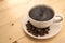 White cup with black steaming coffee on plate with coffee beans