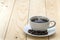 White cup with black steaming coffee on plate with coffee beans