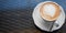 White cup of cappuccino, hot coffee on brown glass table in the cafe, close up, banner