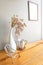 A white cup chinese graphic put beside A white vase with the dried flowers and chair stainlass on a wood table. grey wall in