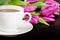 White cup of coffee with bunch of purple tulips on dark background