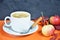 White cup of coffee with cappuccino cream on an orange background with autumn leaves, apples and red berries. Fall