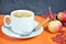 White cup of coffee with cappuccino cream on an orange background with autumn leaves, apples and red berries. Fall