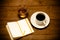 White cup of coffee, cognac in a glass and notebook on old wooden table. Toned
