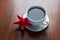 A white cup of coffee with red starfish shell on wooden background