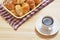 A white cup with coffee is on a saucer, next to a basket of home croissants.