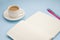 White cup of coffee silver notepad, pink flower on a blue background. Flat lay. copy space