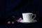 White cup of coffee or tea hot drink in the morning with small pink purple wild flower classical baroque still life with dark blue