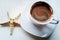 White cup of coffee on white background and starfish, close-up