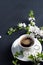 White cup of espresso coffee on a stone table, white cherry blossoms, springtime