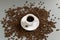 White cup with espresso on a white saucer among coffee beans on a gray background.