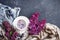 White cup with flowers on a saucer, a bouquet of lilac flowers and a blue drape striped scarf on a dark background