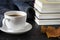 A white cup with a fragrant cove stands on a black table next to books and a blue wool scarf