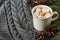 White cup of fresh hot cocoa or hot chocolate with marshmallows on grey knitted background