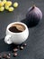 White cup with freshly brewed espresso on a black stone background. Steam rises above the cup. Roasted coffee beans are located