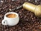 A white cup with freshly brewed espresso stands in coffee beans. Nearby lies a manual bronze coffee grinder. Coffee grains are