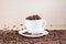 White cup full of roasted coffee beans standing on a white plate on tablemat.