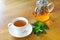 White cup and glass teapot of herbal tea with fresh mint twig on