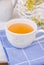 White cup with herbal tea on blue napkin, wicker basket with flowers, pitcher, white table top