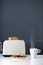 White cup of hot coffee or tea and a toaster with a delicious slice of toasted toast on the kitchen table on gray background.