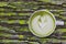 White cup of matcha green tea latte art with foam on rustic moss wooden table with copy space