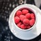 White cup of ripe raspberries, shadows pattern