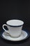 White cup and saucer with blue stripe on black background
