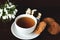 White cup on a saucer with oatmeal cookies near a vase with snowdrops on the table