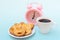 White cup of steaming hot black coffee or hot chocolate, freshly baked heart shaped cookies and pink alarm clock