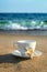 White cup with tea or coffee on sand beach front of sea