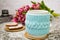 A white cup of tea in a knitted blue case with an old camera and pink flowers tulips and sweets, gingerbread on a textural table