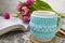White cup of tea in a knitted blue case with an open book and with pink flowers tulips and sweets, with gingerbread on a