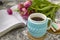 White cup of tea in a knitted blue case with an open book and with pink flowers tulips and sweets, with gingerbread on a