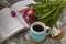 White cup of tea in a knitted blue case with an open book and with pink flowers tulips and sweets, with gingerbread on a textural