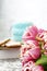 A white cup of tea in a knitted blue case stands on a book and pink flowers, tulips and gingerbread on a texture table