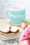 A white cup of tea in a knitted blue case stands on a book and pink flowers, tulips and gingerbread on a texture table. Spring