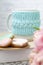 A white cup of tea in a knitted blue case stands on a book and pink flowers, tulips and gingerbread on a texture table. Spring