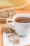 White cup with tea, pieces of brown sugar and homemade cookies with cereals on a white saucer