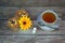 A white cup of tea on a saucer with a spoon and a napkin with two fresh muffins, sugar cubes and a flower bud