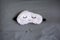 White cute sleep mask made of fluffy faux fur in a cloud shape with closed eyes embroidered on it and custom molded sleep ear