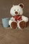 White cute teddy bear with cup sitting on sofa. Soft animal toy. Good morning concept. Childhood background. Romantic gift.